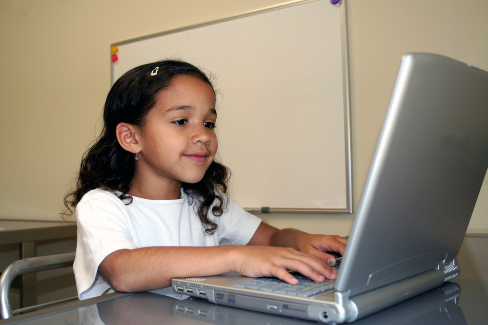 Young girl concentrating on reading exercise on laptop, demonstrating grade-level reading fluency goals