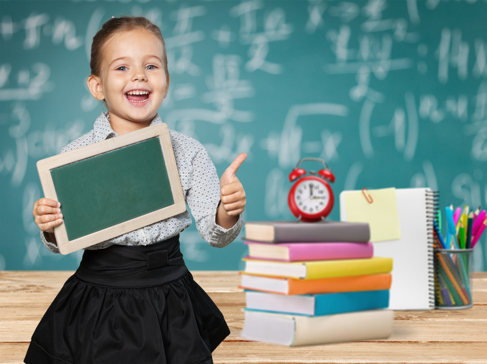 Young girl giving thumbs up with learning materials symbolizing reading levels by grade in a classroom environment
